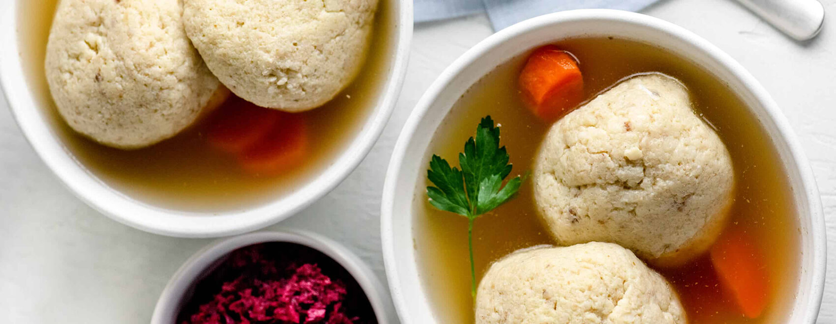 Two white bowls of matzo ball soup in broth with carrots