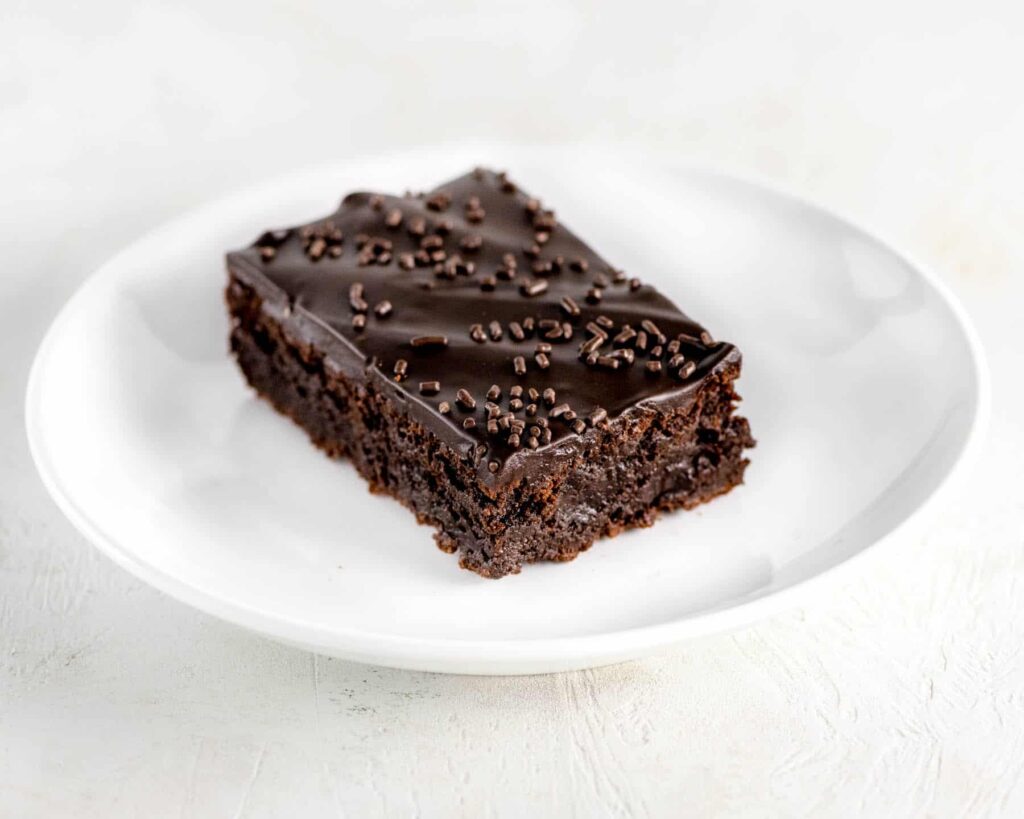 Frosted chocolate fudge brownie with chocolate sprinkles on white plate
