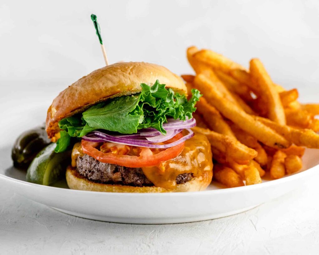 Cheeseburger with lettuce, tomato, onion and fries on a white plate