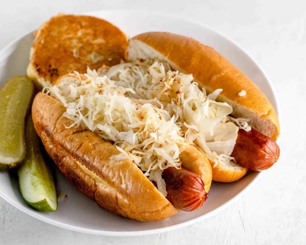 Two hot dogs with grilled sauerkraut and a potato knish on a white plate 