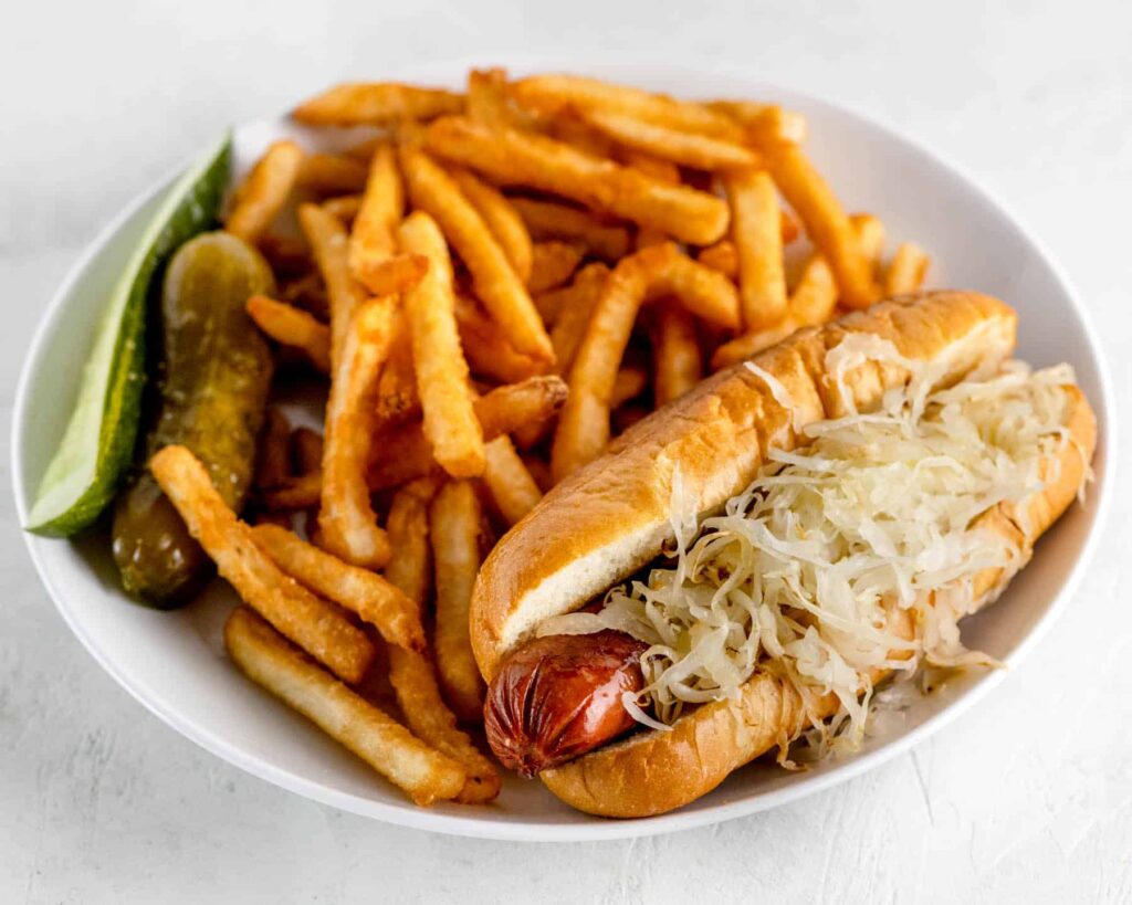 hot dog with grilled sauerkraut on a white plate with fries