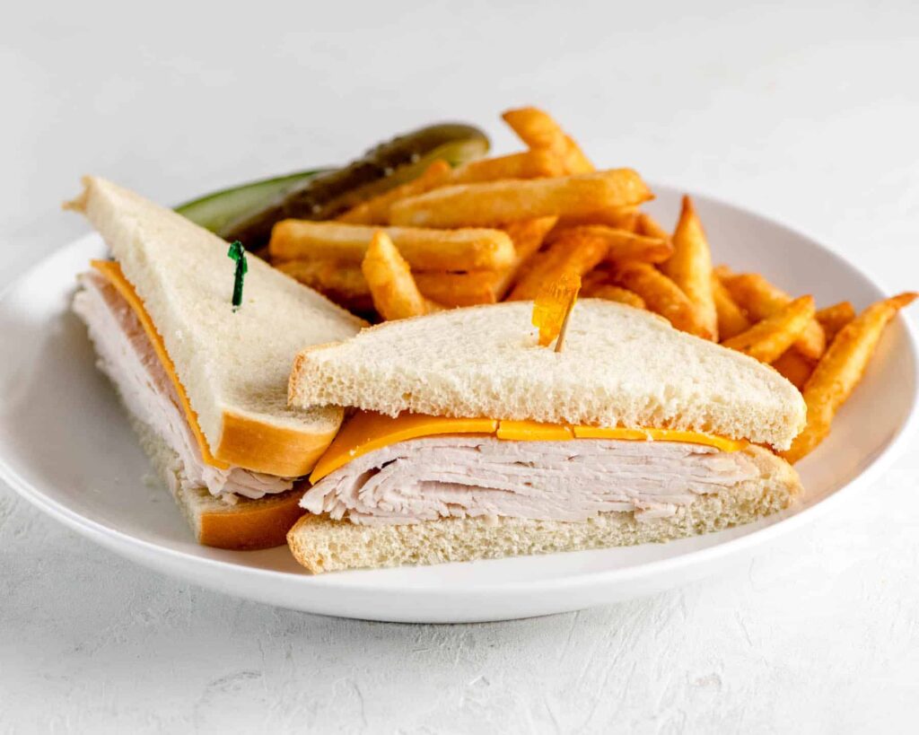kids turkey sandwich with cheese and fries on a white plate