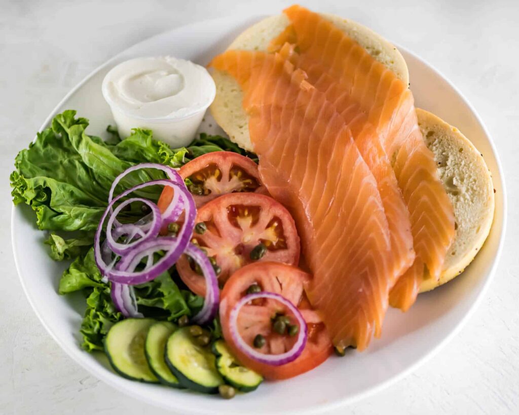 Slices of lox on a New York Bagel with sliced onions, cucumber, tomatoes, capers and cream cheese