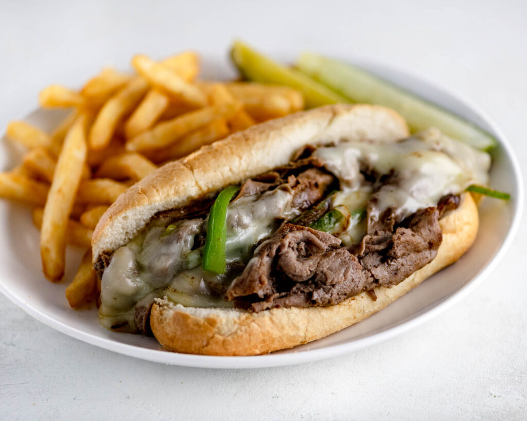 Philly Cheesesteak on a white plate with fries